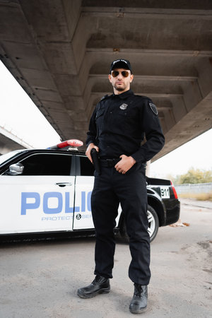 Officer of police holding gun near car on urban street