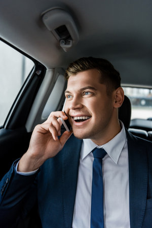 Young businessman smiling while talking on smartphone on back seat of autoの写真素材