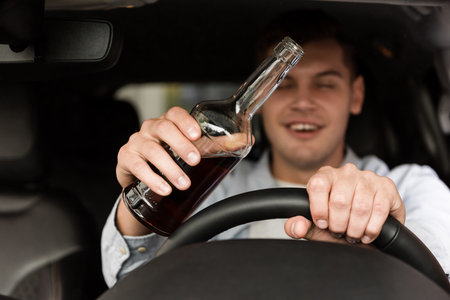 drunk man with bottle of whiskey driving car on blurred backgroundの写真素材