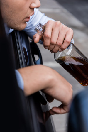 cropped view of man holding bottle of whiskey in car on blurred foreground, bannerの写真素材