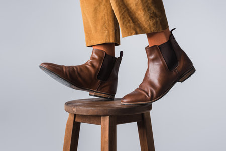 Cropped view of man in orange socks and brown shoes standing on chair isolated on gray