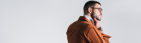 Stylish man in eyeglasses adjusting turtleneck and looking away isolated on gray, bannerの写真素材