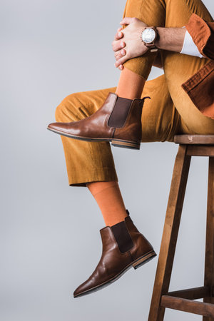 Cropped view of stylish man in brown shoes sitting on wooden chair isolated on grayの写真素材