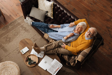 top view of senior couple looking at camera while hugging on couch in living roomの写真素材