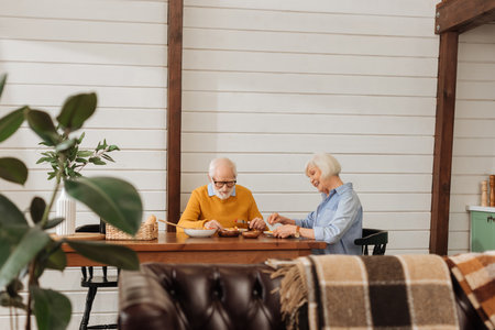 smiling elderly couple eating dinner at table on blurred foreground in kitchenの写真素材