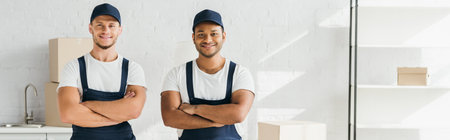 cheerful movers in caps standing with crossed arms in room, banner