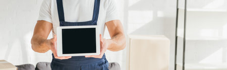 cropped view of mover in uniform holding digital tablet with blank screen near boxes in apartment,...