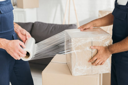 cropped view of movers wrapping box with stretch film