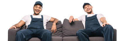 cheerful multicultural movers laughing while sitting on sofa isolated on white, bannerの写真素材