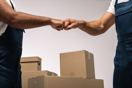 cropped view of workers bumping fists near boxes on grayの写真素材