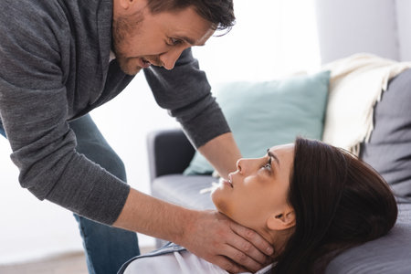 Aggressive man choking wife with bruises on face near couch at home