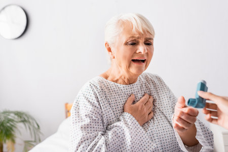 aged woman taking inhaler from nurse while suffering from asthma attack, blurred foreground