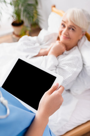 happy elderly woman looking at nurse holding digital tablet with blank screen, blurred backgroundの写真素材