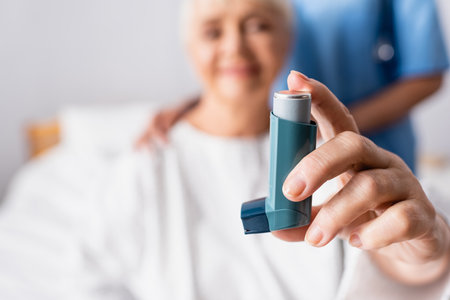 aged woman holding inhaler near nurse in hospital, blurred backgroundの写真素材