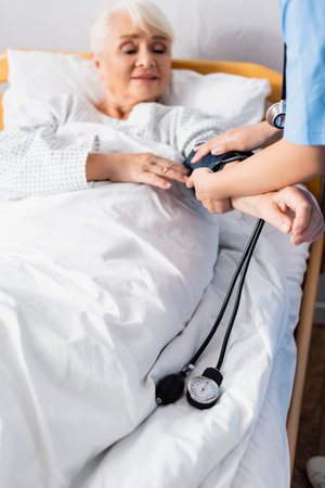 nurse mearing blood pressure of aged woman with tonometer, blurred backgroundの写真素材