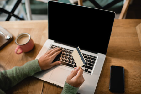 partial view of african american woman holding credit card near laptop with blank screen