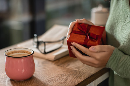 cropped view of african american woman holding wrapped christmas present in cafe