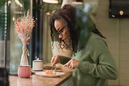 african american woman in eyeglasses holding cutlery near tart on plate