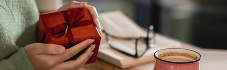 cropped view of african american woman holding wrapped christmas present in cafe, banner