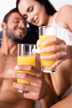close up view of glasses with juice in hands of happy sexy couple in bedroom on blurred backgroundの写真素材