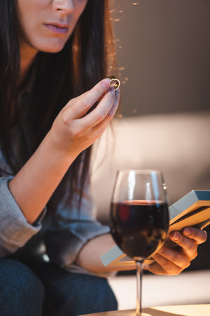 cropped view of woman holding photo frame and wedding ring near glass of red wine on blurred...