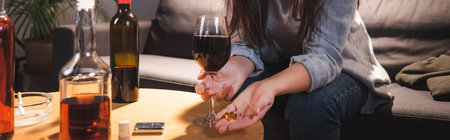 cropped view of woman holding wedding ring and glass of red wine near bottles on blurred foreground, bannerの写真素材