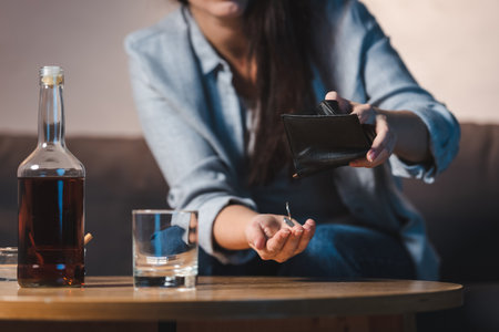 partial view of woman taking coins from wallet near bottle of whiskey on table, blurred backgroundの写真素材