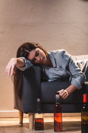 frustrated, drunk woman lying on sofa near bottles on floorの写真素材