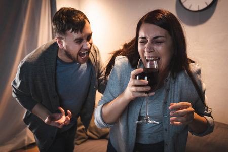 drunk man screaming at alcohol-addicted wife holding wine glass with closed eyesの写真素材