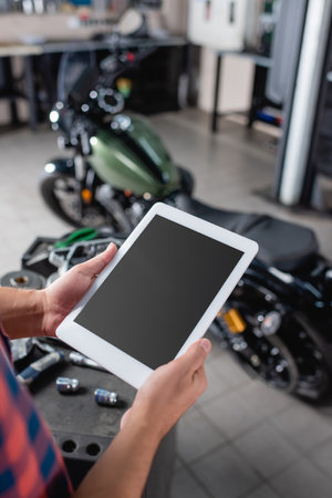 cropped view of repairman holding digital tablet with blank screen near motorcycle on blurred backgroundの写真素材