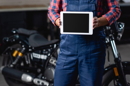 partial view of mechanic holding digital tablet with blank screen near motorbike on blurred backgroundの写真素材
