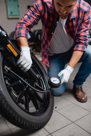 repairman measuring pressure in tire of motorcycle with air gauge