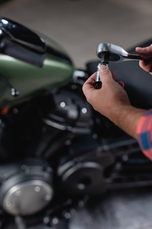cropped view of technician holding socket wrench near motorcycle on blurred background