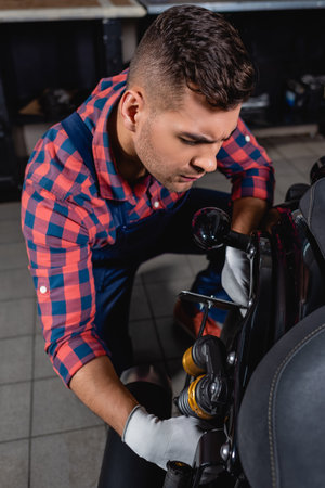 technician in plaid shirt examining shock absorber of motorbike in workshopの写真素材