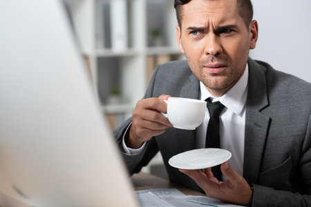 thoughtful businessman holding coffee cup at workplace, blurred foregroundの写真素材