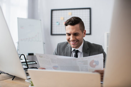 happy trader holding infographics near monitors on blurred foregroundの写真素材
