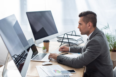side view of trader at workplace near laptop and monitors with blank screen