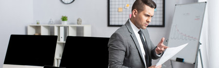 thoughtful trader pointing with finger at document near monitors with blank screen, bannerの写真素材