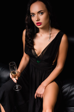 brunette and sexy woman in dress holding glass with champagne isolated on blackの写真素材