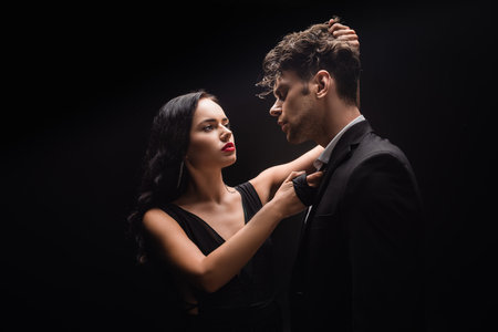brunette woman with red lips looking at man and pulling hair isolated on blackの写真素材