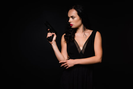 brunette woman in dress holding gun isolated on blackの写真素材