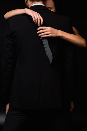 partial view of dangerous woman holding knife behind back of man isolated on black