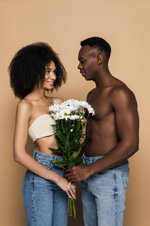 shirtless african american man giving flowers to girlfriend isolated on beigeの写真素材