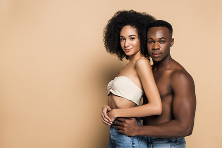 shirtless african american man hugging smiling girlfriend on beigeの写真素材