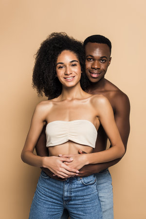 joyful african american woman and man smiling while hugging on beigeの写真素材