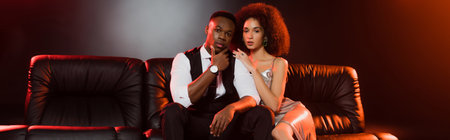 elegant african american couple sitting on couch on black, banner