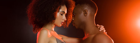 side view of shirtless african american man seducing curly woman on black, bannerの写真素材