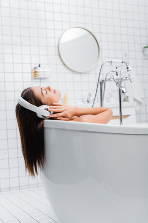 young woman taking bath and listening music in wireless headphones with closed eyesの写真素材
