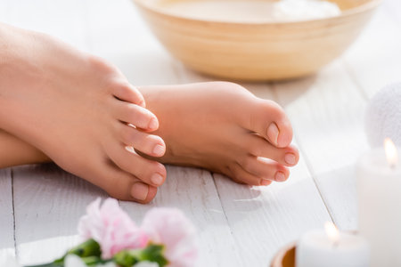cropped view of female feet with pink pastel pedicure on white wooden surface, blurred foregroundの写真素材