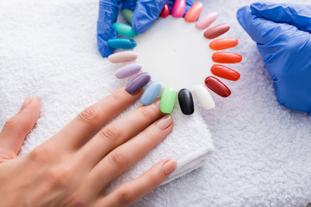 partial view of manicurist holding set of multicolored false nails near hand of clientの写真素材